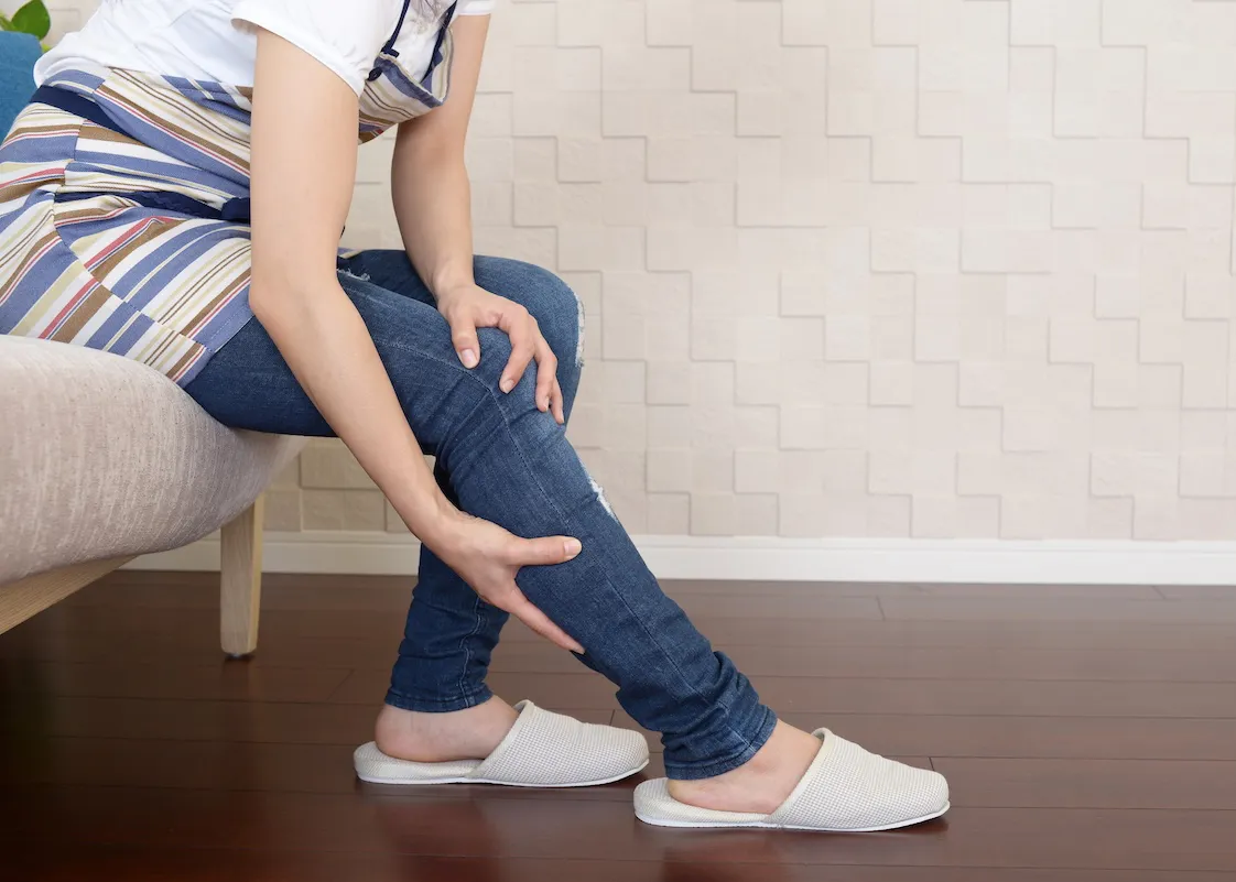 ソファーに座ってふくらはぎをさすっている女性